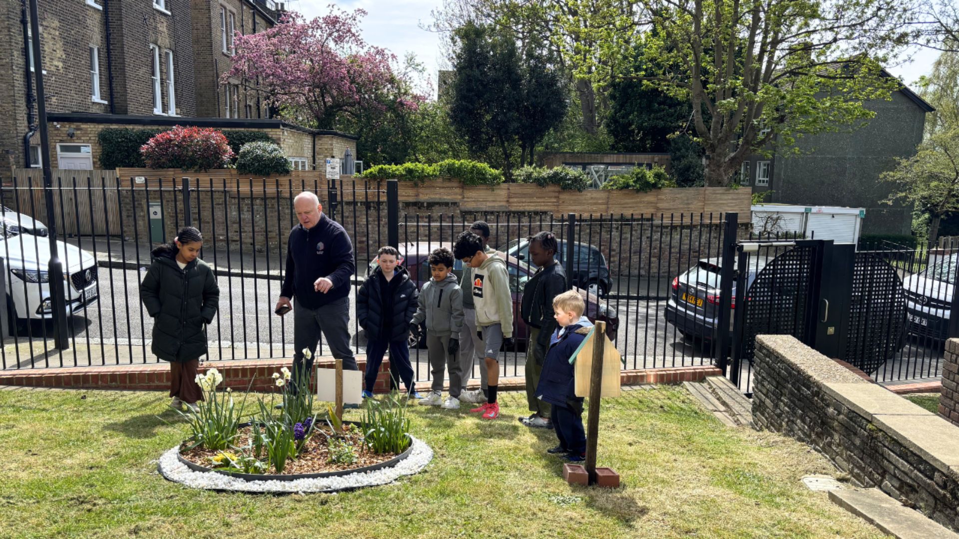 Group gathered around a circular wildflower planting area in a shared green space beside residential buildings.