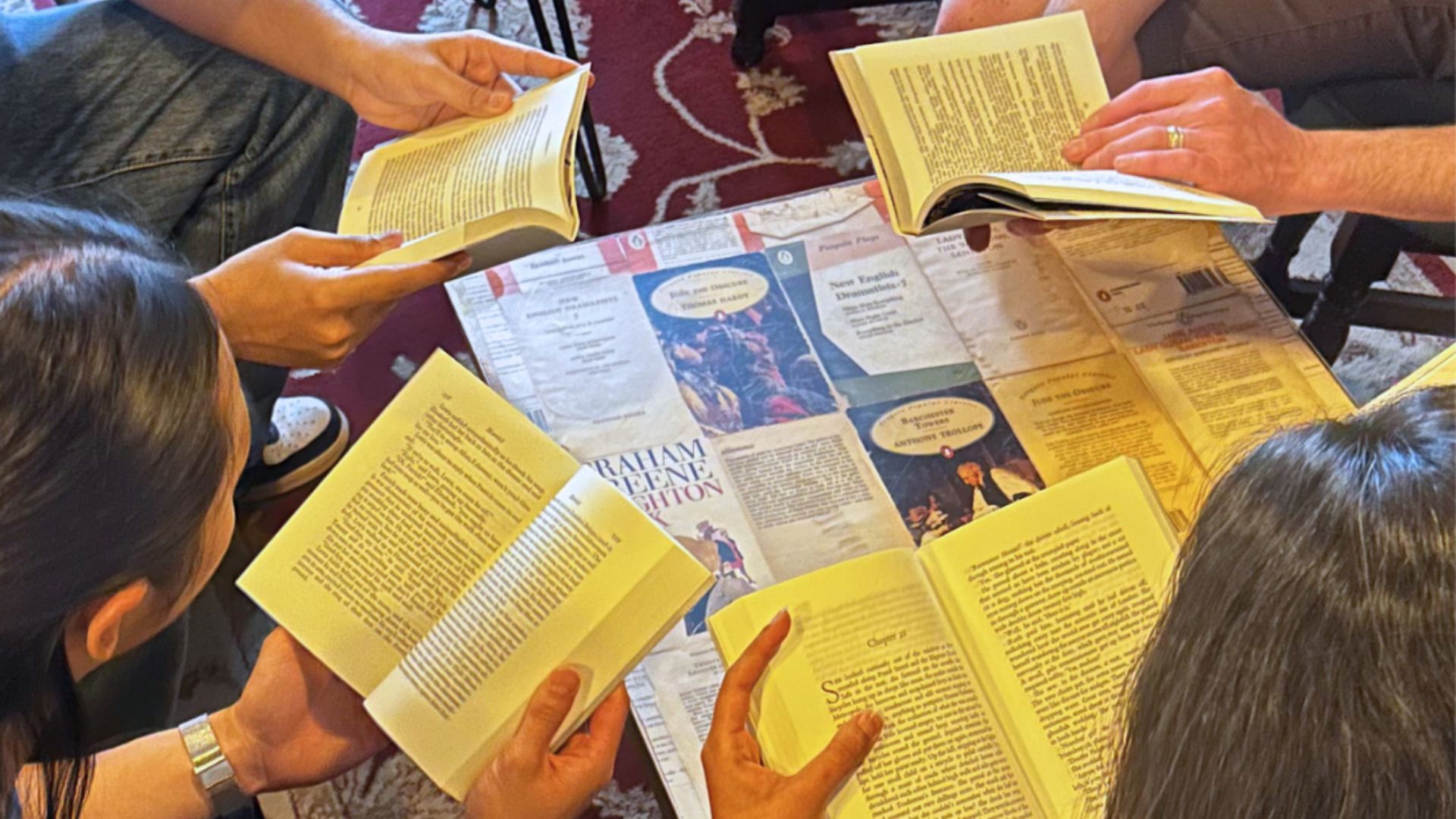 People sitting in a group, each holding and reading an open book, with leaflets and printed materials spread out on the floor in the center.