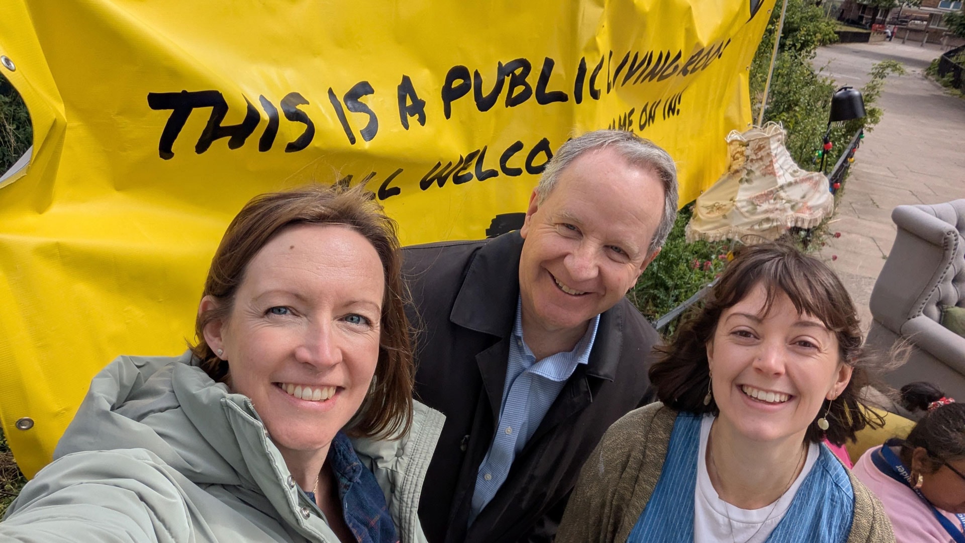 Three smiling people in front of a yellow banner that reads This is a public living room