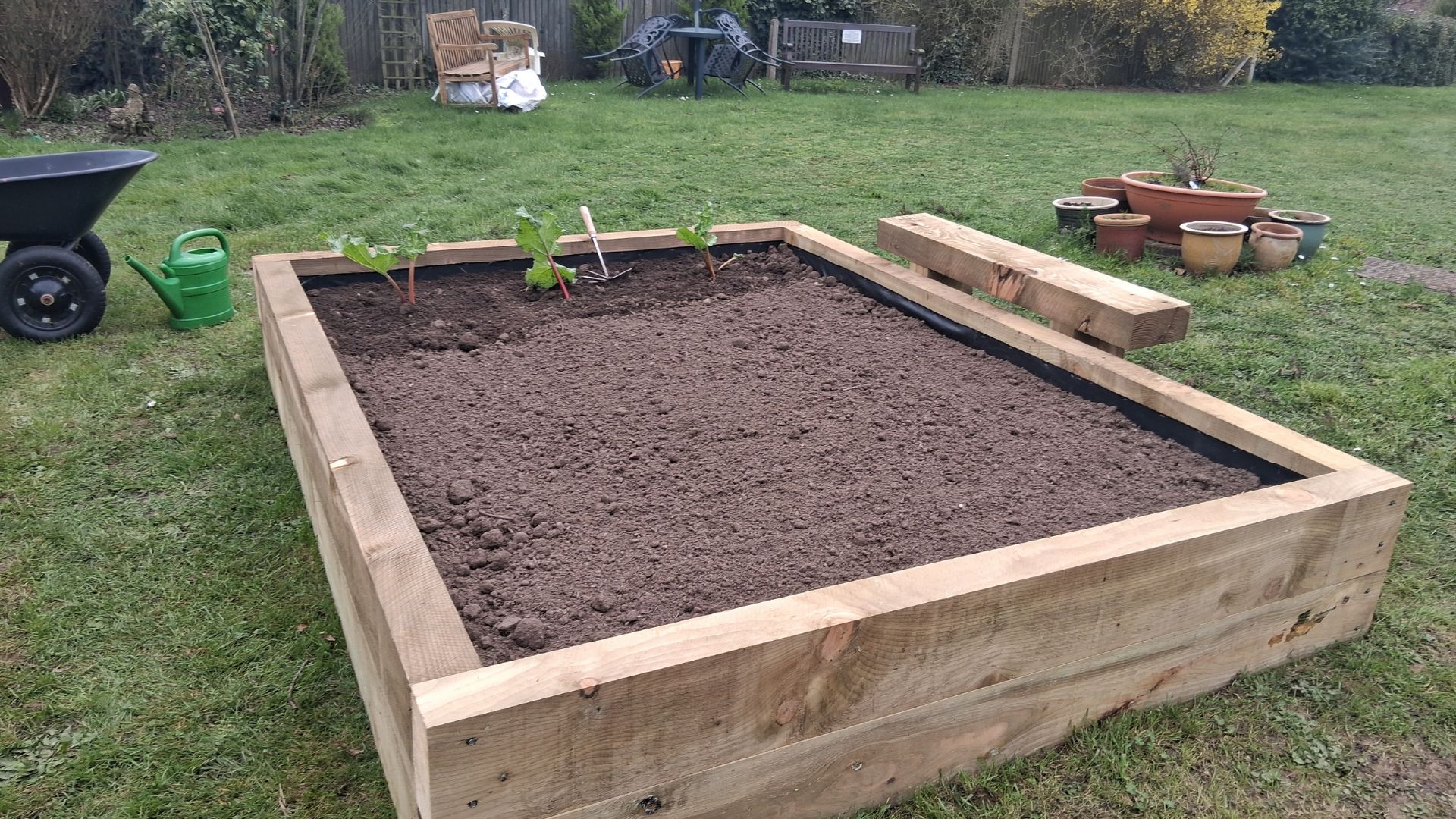 Raised wooden garden bed filled with soil and young plants in a grassy garden.